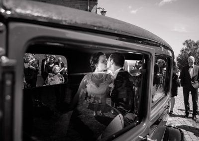 Bryllupsfoto. Brudepar kysser i bil. Billede skudt igennem halvåben bilrude